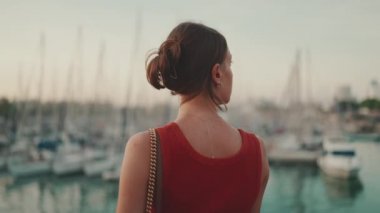 Yakın plan, kız deniz kıyısında duruyor ve yatlarla limana bakıyor. Genç bir kadının yakından çekilmiş portresi sabahları denize bakıyor..