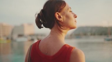 Yakın plan, kız deniz kıyısında duruyor ve körfeze bakıyor ve saçını düzeltiyor. Genç bir kadının yakından çekilmiş portresi sabahları denize bakıyor..