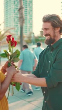 Genç mutlu erkek ve kadının sette buluşurken neşeyle kucaklaşmalarını yakından çekerken, erkek kıza bir buket kırmızı gül verir. Yakın plan, ırklar arası genç çiftin neşeli tarihi