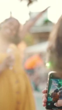 Cep telefonuyla bir kadının fotoğrafını çeken bir adamın yakın planda çekilmiş görüntüsü. Yaklaş, gülümseyen kadın dondurma yiyor ve şehrin arka planında akıllı telefonla filme çekiyor. Arkaplan