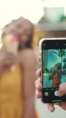 Cep telefonuyla bir kadının fotoğrafını çeken bir adamın yakın planda çekilmiş görüntüsü. Yaklaş, gülümseyen kadın dondurma yiyor ve şehrin arka planında akıllı telefonla filme çekiyor. Arkaplan