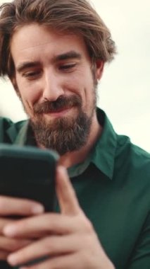 Arka planda sakallı, gülümseyen ve sohbet eden bir adamın yakın çekimi. Cep telefonu kullanan genç ve mutlu bir hippinin önden yakın çekimi.