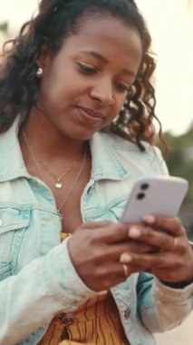 Şehirdeki bir arka planda cep telefonu kullanan uzun kıvırcık saçlı genç bir kadının yakın çekimi. Sosyal ağlarda gezinen, internetten alışveriş yapan kızlara yakın çekim