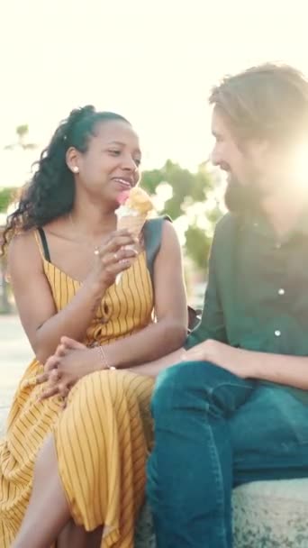 垂直ビデオ 都会の背景でアイスクリームを食べる幸せな異人種間のカップルのクローズアップ肖像画 男性と女性の試飲アイスクリームのクローズアップ — ストック動画