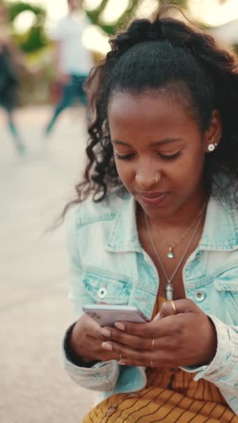 縦型映像 都会の風景を背景に携帯電話で長い巻き毛の若い女性の閉鎖 スマートフォンに音声メッセージを送る少女のクローズアップ — ストック動画