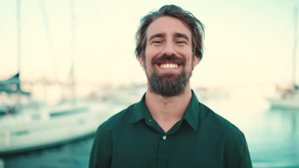 一个面带微笑的男人的特写 他的胡子在堤岸上 在游艇的背景上 快乐的年轻嬉皮士男性在镜头前的前部特写 — 图库视频影像