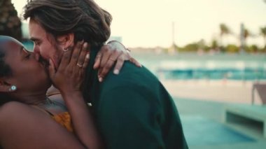 Yakından, bir erkek ve bir kadın buluştuklarında öpüşüyor ve neşeyle iletişim kuruyorlar. Irklar arası mutlu bir çiftin yakın çekimi. Kamera insanların etrafında dönüyor.