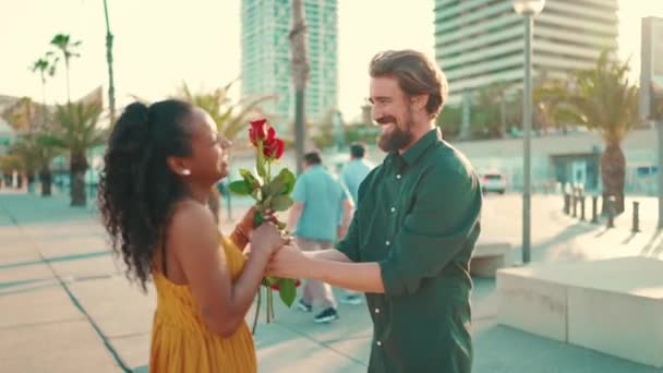 年轻快乐的男女在路堤上欢欢喜喜地拥抱在一起 男人送给女孩一束红玫瑰 一个年轻的跨种族夫妇欢欢喜喜的约会 — 图库视频影像