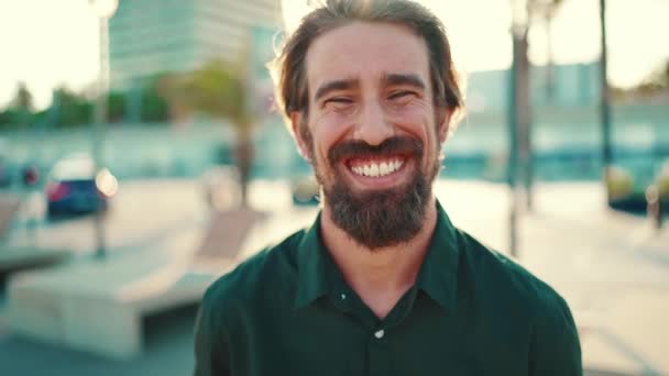 城市背景上一个留着胡子的笑脸男子的肖像 年轻快乐的嬉皮士男性在镜头前的前部特写 — 图库视频影像