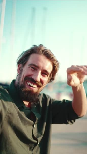 垂直录像 一个满脸笑容的男人 留着胡子 在堤岸上 在游艇的背景上聊天的合影 用手机对快乐的年轻男性嬉皮士进行前部特写 — 图库视频影像