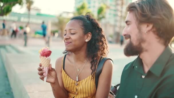 都市部の背景にアイスクリームを食べる笑顔異人種間のカップルのクローズアップ肖像画 男性と女性の試飲アイスクリームのクローズアップ — ストック動画