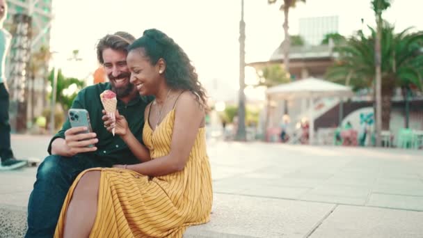 一个快乐的男人和一个微笑的女人在智能手机上观看视频 一对快乐的跨种族年轻夫妇在城市背景的手机上浏览照片的特写 — 图库视频影像