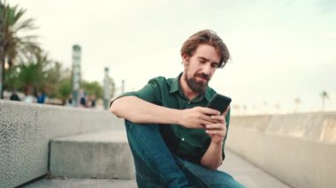 Arka planda sakallı, gülümseyen bir adamın görüntüsü. Cep telefonu kullanan genç ve mutlu erkek hippilerin önden yakın çekimi.