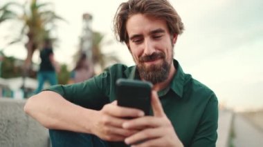 Arka planda sakallı, gülümseyen bir adamın yakın plan portresi. Cep telefonu kullanan genç ve mutlu erkek hippilerin önden yakın çekimi.