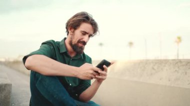 Arka planda sakallı, gülümseyen bir adamın görüntüsü. Cep telefonu kullanan genç ve mutlu erkek hippilerin önden yakın çekimi.