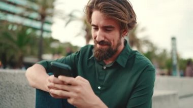 Arka planda sakallı, gülümseyen bir adamın yakın plan portresi. Cep telefonu kullanan genç ve mutlu erkek hippilerin önden yakın çekimi.