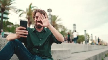 Arka planda sakallı, gülümseyen bir adamın görüntüsü. Cep telefonu kullanan genç ve mutlu erkek hippilerin önden yakın çekimi.