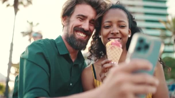 スマートフォンで動画を見ている幸せな男と笑顔の女性の肖像画を閉じます 都市の背景に携帯電話で楽しい若い異人種間カップルのブラウジング写真のクローズアップ — ストック動画