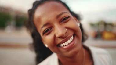 Çeşmenin önünde uzun kıvırcık saçlı, gülümseyen genç bir kadının yakın plan portresi. Kameraya gülümseyen kıvırcık saçlı bir kızın yakın çekimi.