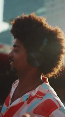 Kulaklıkla müzik dinleyen ve şehir arka planında dans eden neşeli, Afro-Amerikan bir adamın yakın çekimi. Yaşam tarzı konsepti. Arka plan Yavaş çekim