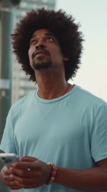 Yakından bakınca, açık mavi tişörtlü Afro-Amerikalı genç bir adam modern şehrin caddesine çıkıyor ve elinde akıllı telefon ile şehirdeki elektronik haritalı bir adrese bakıyor. yavaş çekim