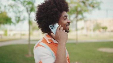 Parktaki yolda yürürken ve akıllı telefondan konuşan Afro-Amerikan genç adamın yakın çekimi. Cep telefonuyla duygusal konuşan bir adam. Yaşam tarzı konsepti. Yavaş çekim