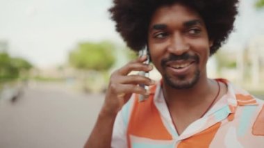 Parktaki yolda yürürken ve akıllı telefondan konuşan Afro-Amerikan genç adamın yakın çekimi. Cep telefonuyla duygusal konuşan bir adam. Kamera adamın etrafında dönüyor. Yavaş çekim