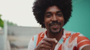 Tişört giyen, açık mavi duvar arkaplanına video mesajı gönderen neşeli, Afro-Amerikan bir adamın yakın çekimi. Yaşam tarzı konsepti. Yavaş çekim