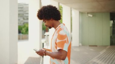 Gömlekli genç bir Afro-Amerikalı gün doğumunda sosyal ağlarda cep telefonuyla yürüyüş hakkında yazıyor. Yaşam tarzı konsepti. Yavaş çekim