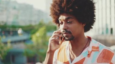 Gömlek giyen ve akıllı telefondan konuşan Afrikalı genç bir adamın yakın çekimi. Yaşam tarzı konsepti. Yavaş çekim geri aydınlatma. Yavaş çekim