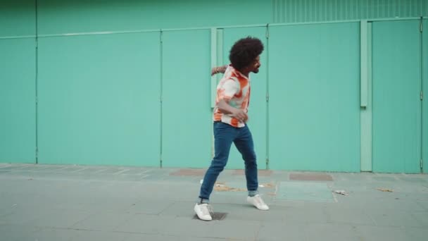 快乐的年轻非洲裔美国人 身穿衬衫 用无线耳机听音乐 在浅蓝色的墙壁背景下跳舞 生活方式的概念 慢动作 — 图库视频影像