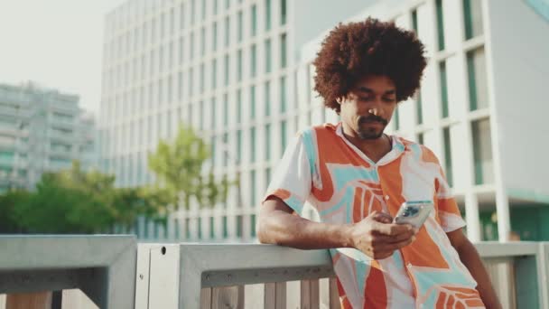 身穿衬衫的年轻的非裔美国人在社交网络上写着城市街道背景的手机 镜头向前移动接近那个人 慢动作 — 图库视频影像