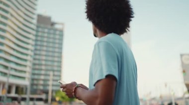 Yakından bakınca, açık mavi tişörtlü Afrikalı genç bir adam modern şehrin caddesinde duruyor ve elinde akıllı bir telefonla telefon ile şehrin elektronik haritalı adresini arıyor..