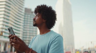 Yakından bakınca, açık mavi tişörtlü Afrikalı genç bir adam modern şehrin caddesinde duruyor ve elinde akıllı bir telefonla telefon ile şehrin elektronik haritalı adresini arıyor..