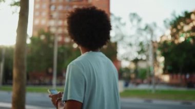 Yakından bakınca, açık mavi tişörtlü Afro-Amerikan bir adam elinde akıllı telefonuyla modern şehrin sokaklarında geziyor ve telefon ekranında elektronik haritalı bir adres arıyor. yavaş çekim