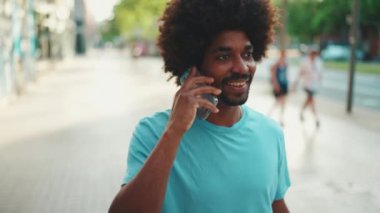 Açık mavi tişörtlü, gülümseyen ve cep telefonuyla konuşan Afro-Amerikan genç adamın yakın çekimi. yavaş çekim