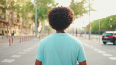 Açık mavi tişörtlü Afro-Amerikan genç adam yaya geçidinde duruyor. Arkadan bak. Yavaş çekim