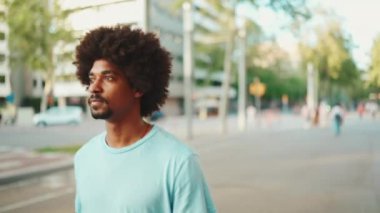 Açık mavi tişörtlü genç Afro-Amerikan bir adamın modern şehir arka planında caddede yürümesi. Yavaş çekim