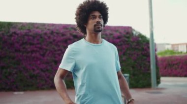 Arkadaki duvarda mor çiçeklerle kaplanmış, Afro-Amerikalı genç bir adamın ön portresi. Yaşam tarzı konsepti. Yavaş çekim