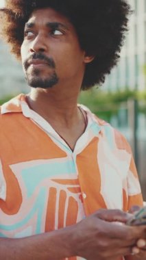 Yakından bakınca, tişört giyen genç Afrikalı Amerikalı adam sosyal ağlarda şehir arka planında cep telefonuyla yazıyor. Kamera ileri doğru hareket ediyor. Yavaş çekim