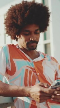 Yakından bakınca, tişört giyen genç Afrikalı Amerikalı adam sosyal ağlarda şehir arka planında cep telefonuyla yazıyor. Kamera ileri doğru hareket ediyor. Yavaş çekim