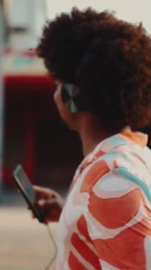 Kulaklıkla müzik dinleyen ve şehir arka planında dans eden neşeli, Afro-Amerikan bir adamın yakın çekimi. Yaşam tarzı konsepti. Arka plan Yavaş çekim