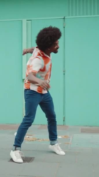 Vertical Video 快乐的年轻非洲裔美国人 身穿衬衫 用无线耳机听音乐 在浅蓝色的墙壁背景下跳舞 慢动作 — 图库视频影像