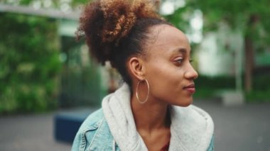 Kot ceketli, at kuyruklu Afro-Amerikan bir kadının yakın plan portresi başını çevirir ve gülümser. Yavaş çekim