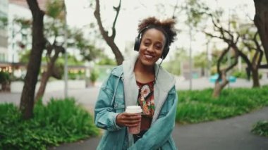 At kuyruklu, kot ceketli, gülen Afrikalı bir kız. Ulusal modelde giyinmiş, sokakta yürüyor kulaklıkla müzik dinliyor ve dans ediyor. Yavaş çekim