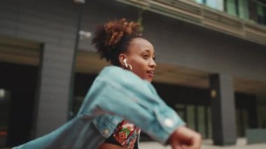 Yakından bakınca, at kuyruklu, kot ceketli gülümseyen Afrikalı bir kız. Üzerinde ulusal bir model var. Kulaklıkla müzik dinliyor ve dışarıda dans ediyor. Kamera yaklaşıyor.