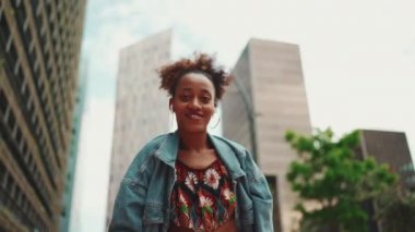 At kuyruklu, kot ceketli, gülen Afrikalı bir kız. Ulusal modelde giyinmiş kulaklıkla müzik dinliyor ve dışarıda dans ediyor. Yavaş çekim
