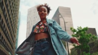 Yakından bakınca, at kuyruklu, kot ceketli gülümseyen Afrikalı bir kız. Üzerinde ulusal bir model var. Kulaklıkla müzik dinliyor ve dışarıda dans ediyor. Kamera yaklaşıyor.