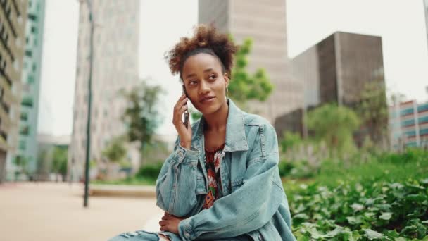 身穿斜纹棉布夹克 身穿马尾辫的美丽的非洲女孩在现代城市背景下通过手机交谈 慢动作 — 图库视频影像