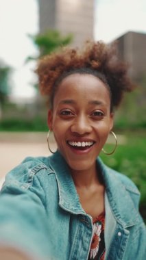 Kapanış portresi at kuyruklu, kot ceket giyen, sabah kahvesiyle oturan ve modern şehir arka planında video görüşmeleri yapan sevimli Afrikalı kız. Yavaş çekim